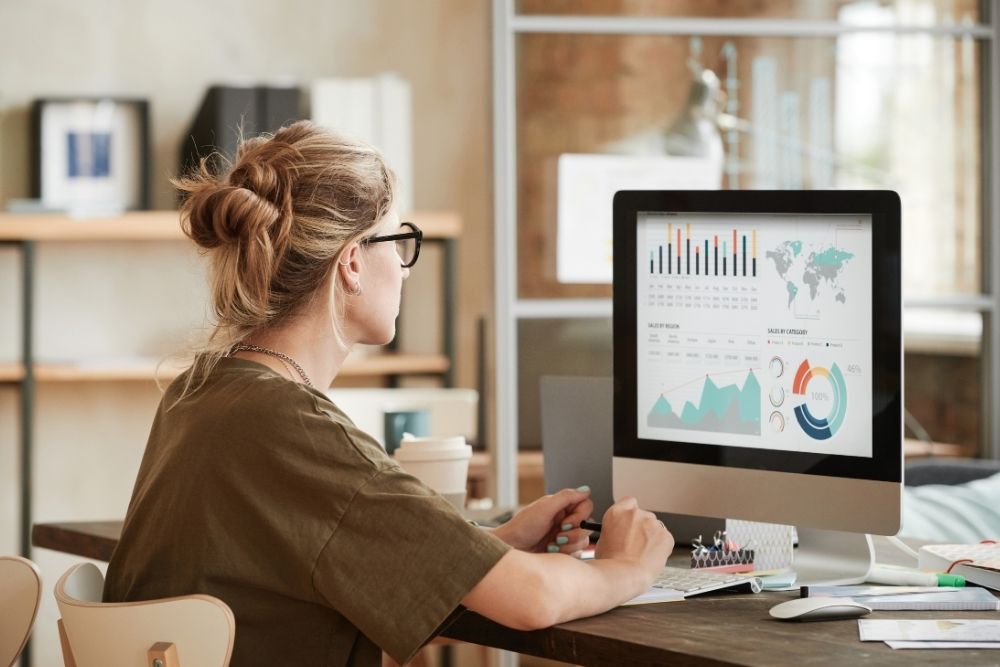 mulher observa gráficos coloridos e mapas exibidos em tela de computador.